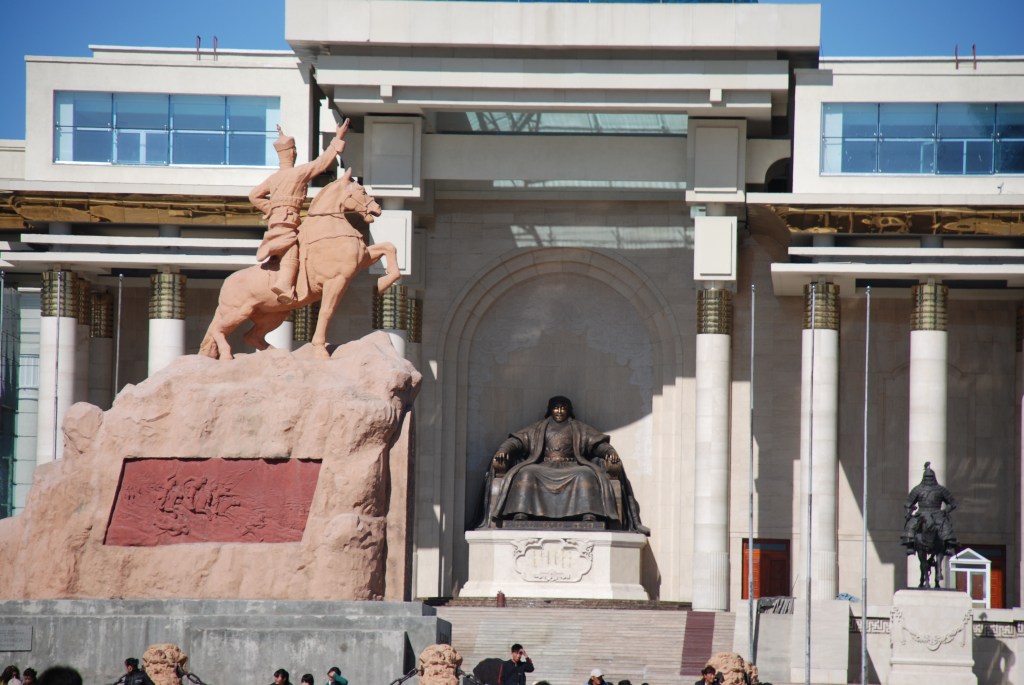 Sükhbaatar Meydanı’nda Damdin Sükhbaatar’ın atlı heykeli ve Hükümet Sarayı önündeki Cengiz Han heykeli